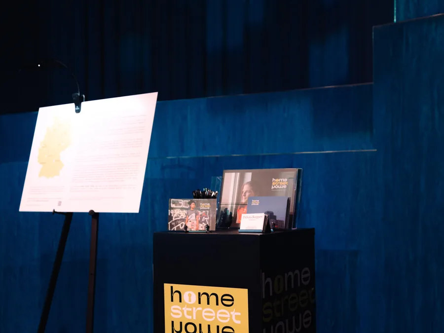 Beleuchtete Ausstellungstafel mit Deutschlandkarte neben einem Pult mit Begleitmaterial, HOME STREET HOME